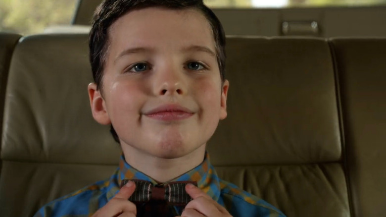 Young Sheldon proudly wearing a bow tie in the backseat of a car in Young Sheldon