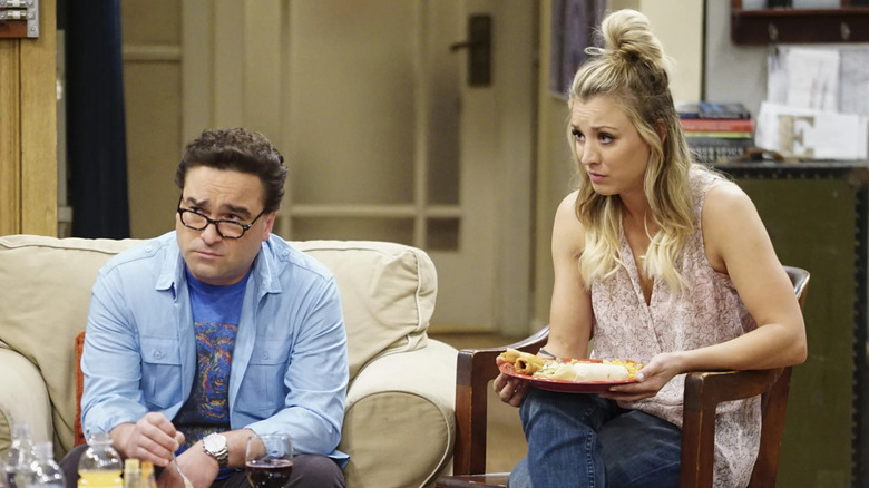 Leonard on the couch and Penny in a chair both eating and looking confused on The Big Bang Theory