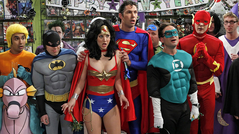 The cast of The Big Bang Theory standing in a comic book store, dressed as superheroes.