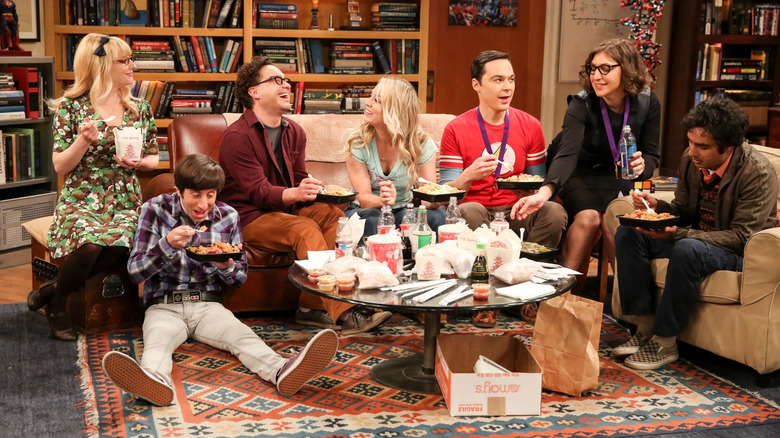 The cast of The Big Bang Theory sitting in their living room, sharing a meal of takeout Chinese food,