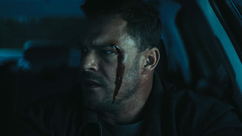 Alan Ritchson's Jack Reacher sits bloodied in the driver's seat of a car in Reacher