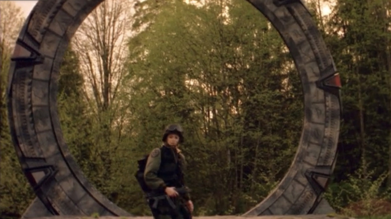 Amanda Tapping's Samantha Carter steps out of the portal  in a wooded area in Stargate SG-1