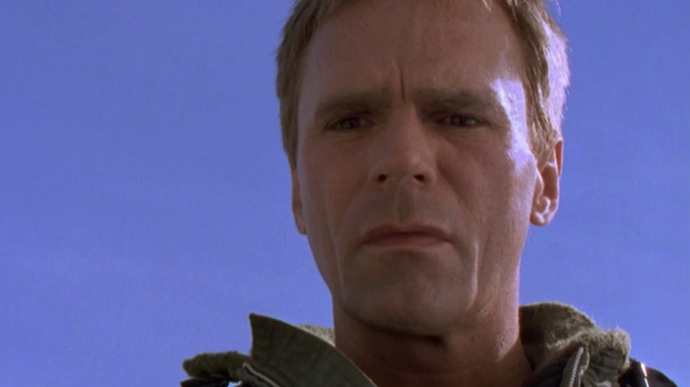 Richard Dean Anderson's Jack O'Neill looks down with a clear blue sky in the background in Stargate SG-1