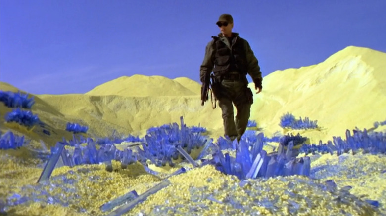 Richard Dean Anderson's Jack O'Neill explores a yellow planet with blue crystals on the ground in Stargate SG-1