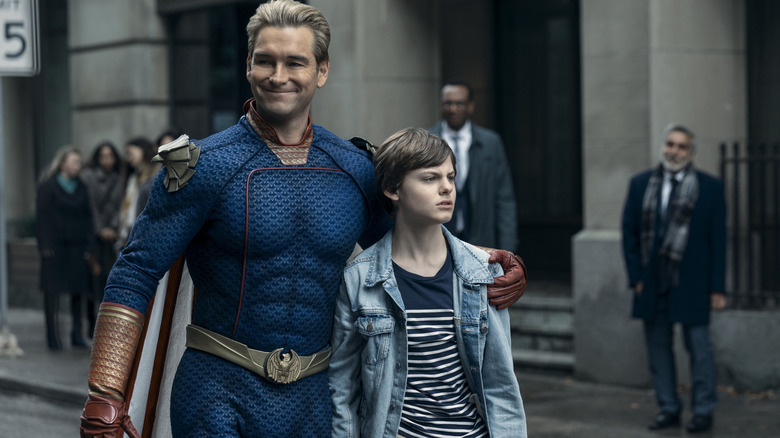 Antony Starr as Homelander embracing his super-powered son Ryan (Cameron Crovetti) while walking through the streets