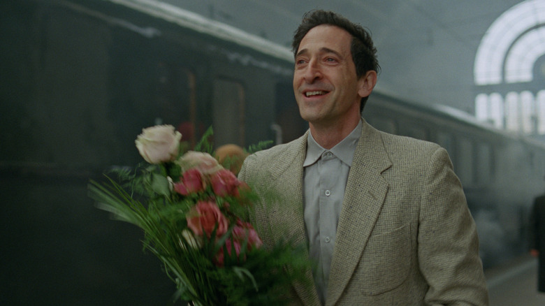 Adrien Brody as architect László Tóth holding a bunch of flowers in The Brutalist