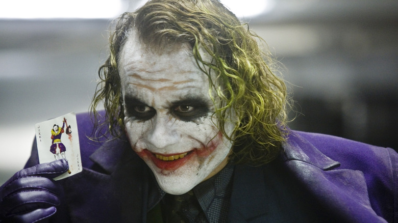 Heath Ledger as Joker holding a joker card in The Dark Knight