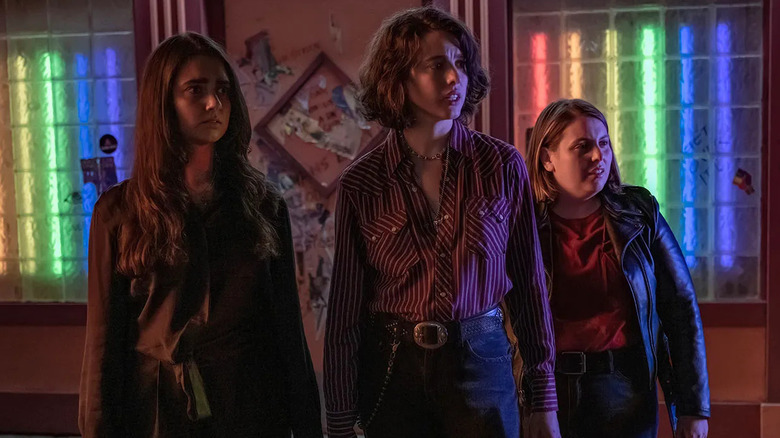 Geraldine Viswanathan, Margaret Qualley, and Beanie Feldstein looking concernedly outside a bar in Drive-Away Dolls