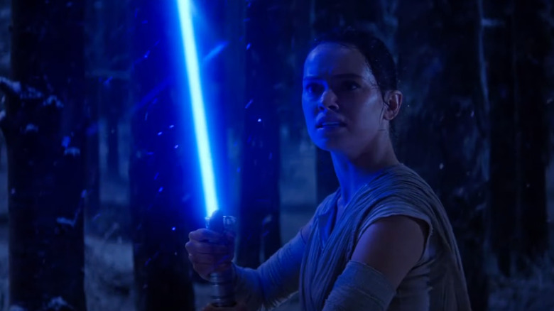 Rey holds a lightsaber in The Force Awakens