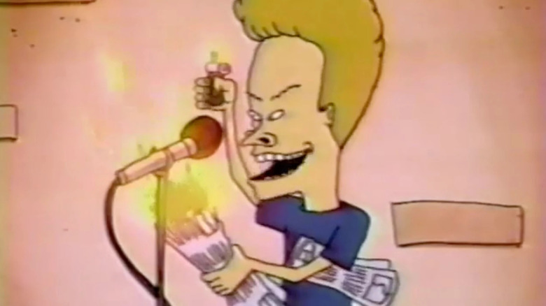 Beavis, lighting a newspaper roll on fire, next to a mic stand.