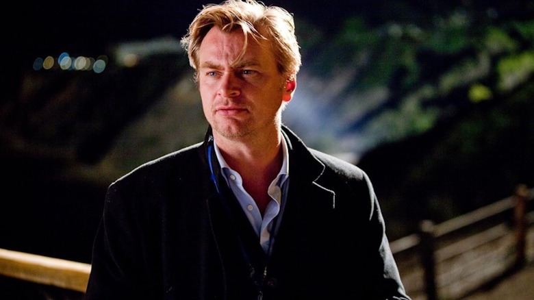 Christopher Nolan está afuera con una chaqueta holgada y una camisa abotonada.