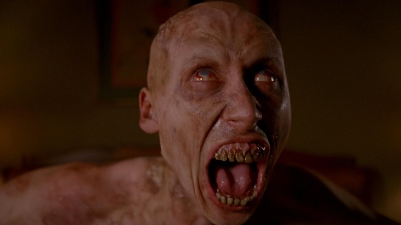 A monstrous person with veiny skin, pale eyes, and messed up teeth wailing in American Horror Story