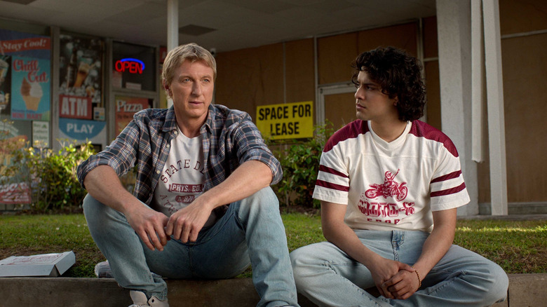 Johnny Lawrence and Miguel Diaz sitting on a curb and talking in Cobra Kai