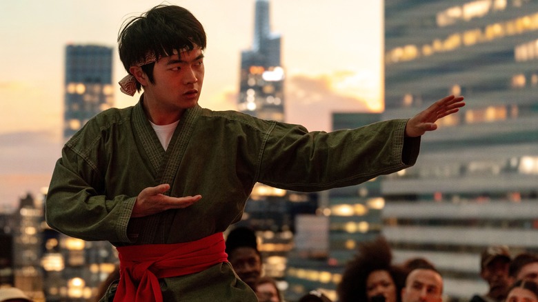 Li Fong doing karate on a rooftop with a crowd watching in the background in Karate Kid: Legends