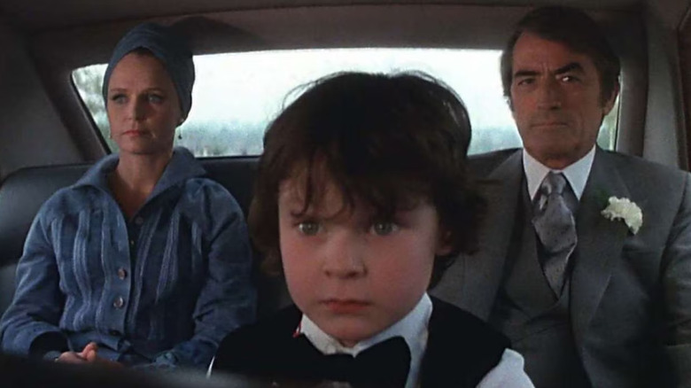 Katherine Thorn and Robert Thorn sitting on either side of a disturbed looking Damien in The Omen.