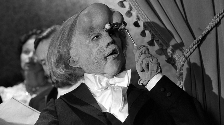 John Hurt sebagai John Merrick memandang pantomim melalui kacamata opera di The Elephant Man