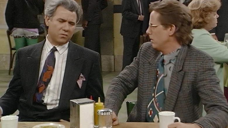 John Larroquette as Reinhold Daniel Fielding Elmore sitting at a table on Night Court