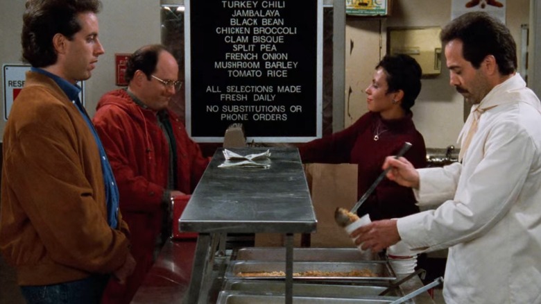 Jerry Seinfeld and Jason Alexander's George stand awkwardly on the opposite side of a deli counter from the Soup Nazi (Larry Thomas) and his coworker in Seinfeld