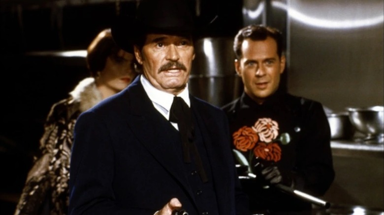 James Garner mengacungkan pistol sebagai wyatt earp sebagai bruce willis yang tersenyum saat tom mix terlihat di matahari terbenam