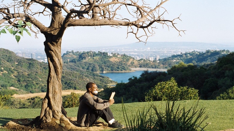 Jack McCall undrneath a leafless tree, tape over his mouth. He reads.