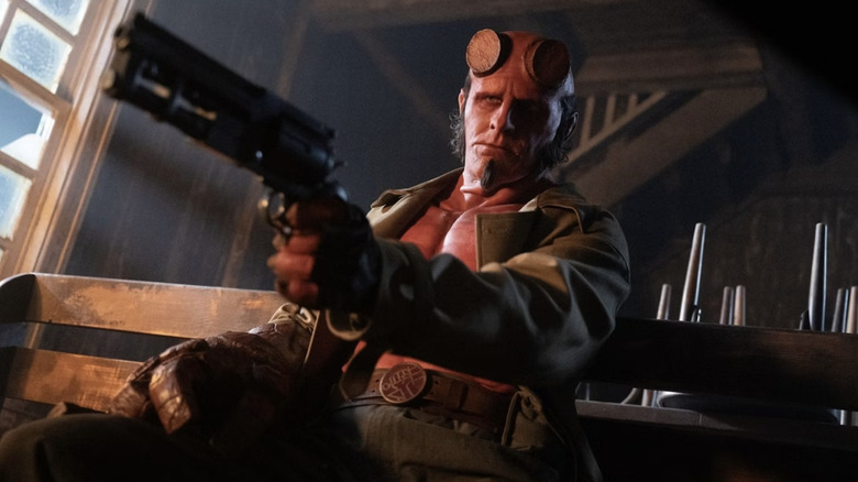 Hellboy apontando arma e sentado na igreja em Hellboy: o homem torto