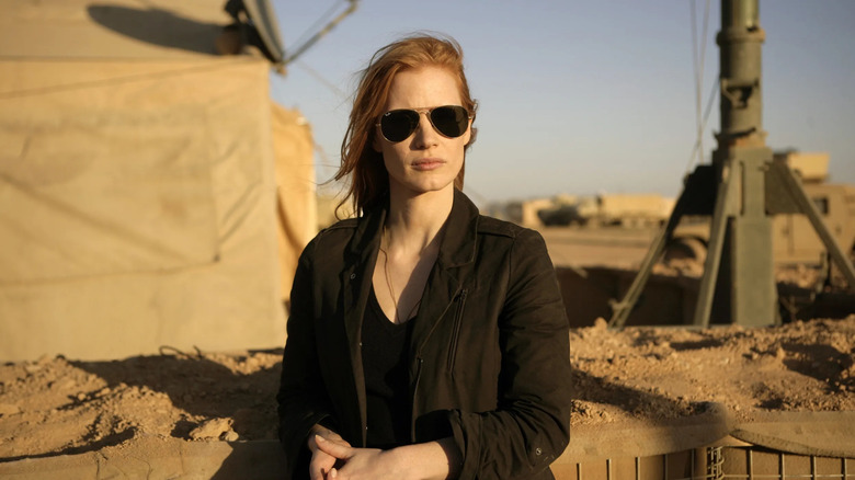 Maya (Jessica Chastain) stares pensively wearing aviator sunglasses against a desert background with military equipment in Zero Dark Thirty