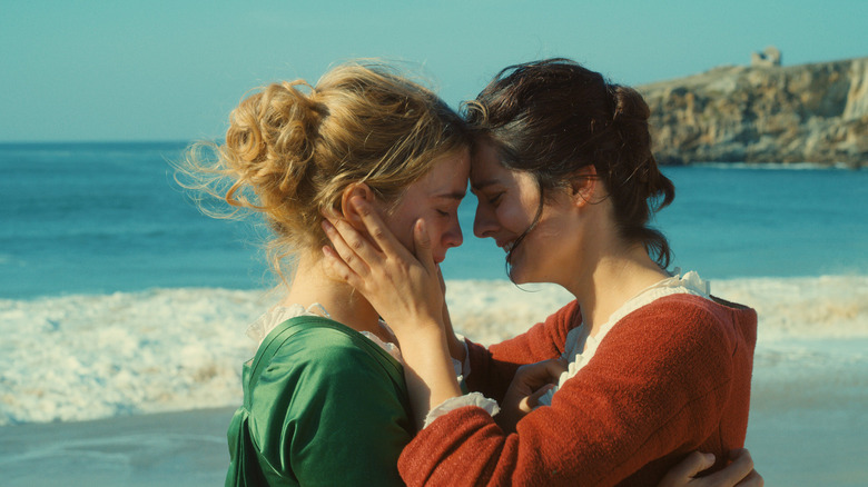 Marianne (Noémie Merlant) cradles Héloïse's face (Adèle Haenel) while standing in front of the ocean and rocky cliffs in Portrait of a Lady on Fire