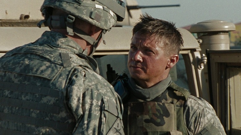 Staff Sergeant William James (Jeremy Renner) stands in front of a military helicopter in The Hurt Locker, wearing a military uniform with a serious and focused expression