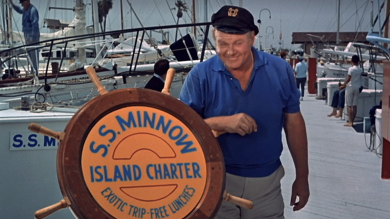 Alan Hale Jr.'s Captain Jonas Grumby stands next to a boat wheel bearing the name of the S S Minnow in Gilligan's Island