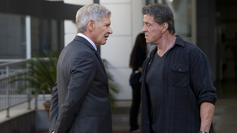 Agent Max Drummer in a suit, talking to a tough-faced Barney in a scene from The Expendables 3