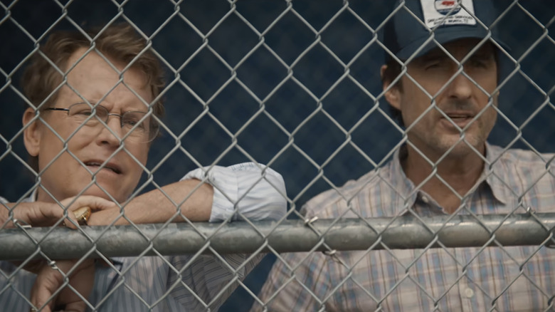 Greg Kinnear's Coach Jon Kelly stands alongside Luke Wilson's Bobby Ratliff behind a mesh fence in You Gotta Believe