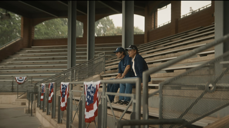 Greg Kinnear's Coach Jon Kelly sits in the bleachers of a baseball field alongside Luke Wilson's Bobby Ratliff in You Gotta Believe