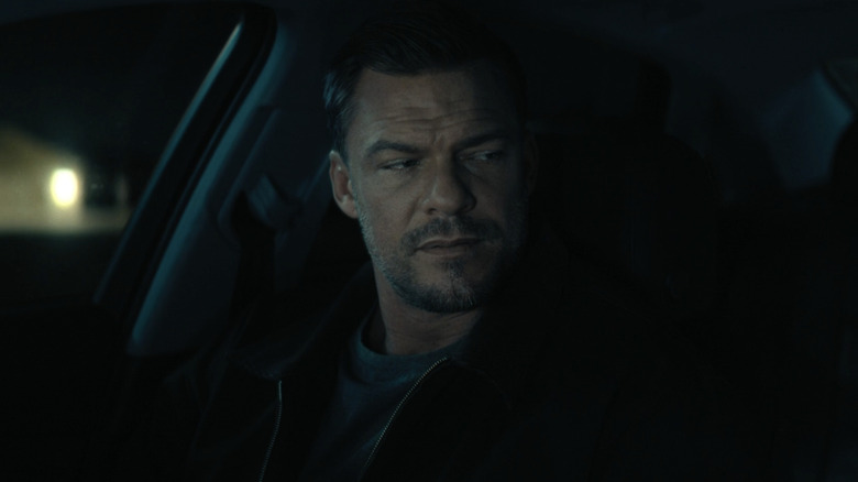 Alan Ritchson's Jack Reacher looks to his left while sitting in the passenger seat of a car in Reacher