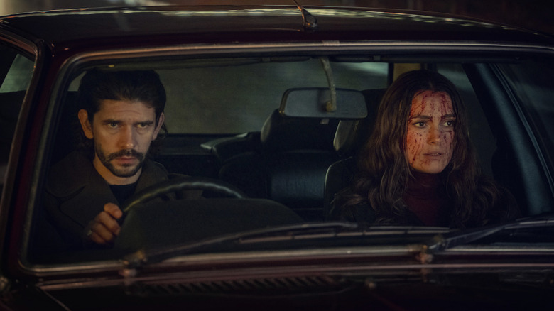 Keira Knightley's Helen Webb sits covered in blood in the passenger seat of a car alongside Ben Whishaw's Sam Young in Black Doves