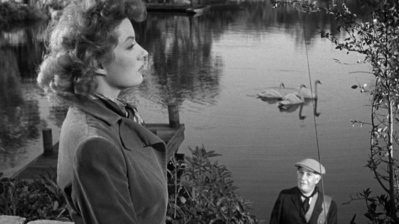 Greer Garson sebagai Kay Miniver melihat ke kejauhan sementara Henry Travers ketika Tuan Ballard mengawasinya di depan sebuah danau di Mrs. Miniver