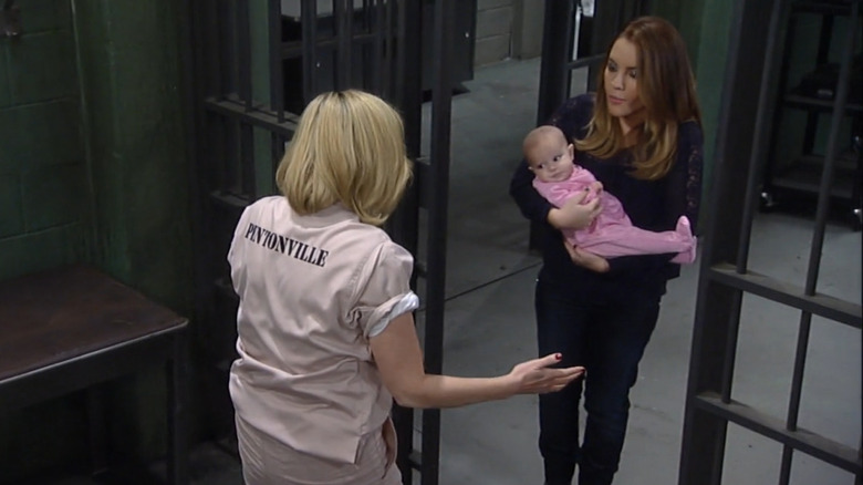 A woman in a pink prison jumper being presented with an infant by another woman, all from an episode of General Hospital.