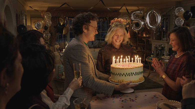 Margaret looking at a lit birthday cake, surrounded by friends in Here