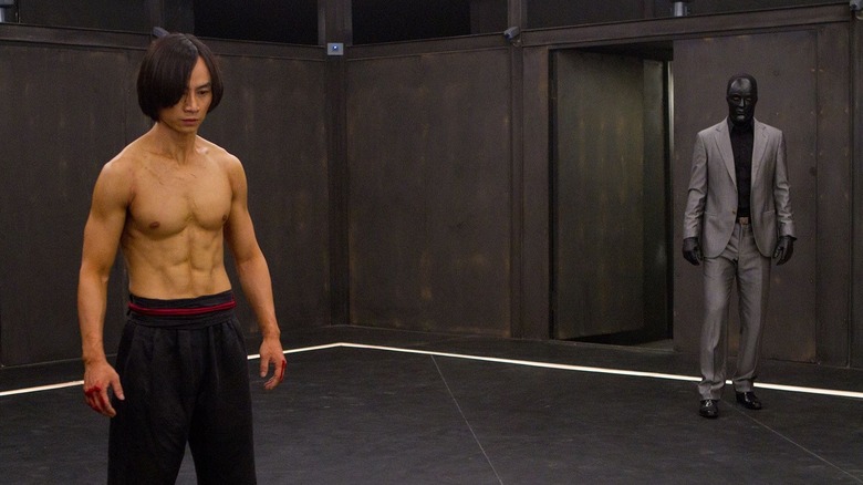 Tiger Chen, shirtless, about to fight a man in a suit, his face painted black.