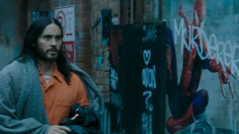 Jared Leto as Michael Morbius, wearing a prison jumpsuit and walking past graffiti of Spider-Man in Morbius