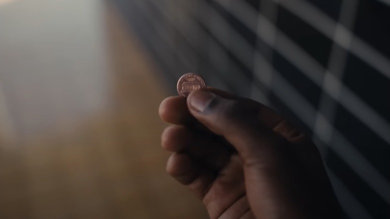 A hand holds a penny in Nickel Boys