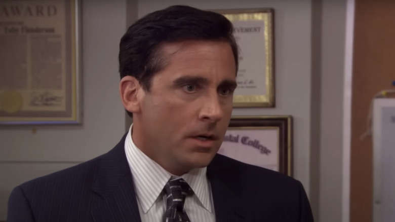 Michael Scott stands in the Dunder Mifflin office in a suit in The Office