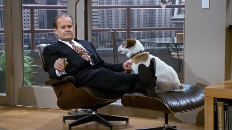 Frasier wearing a suit, reclining in a chair with Eddie the dog sitting at his feet