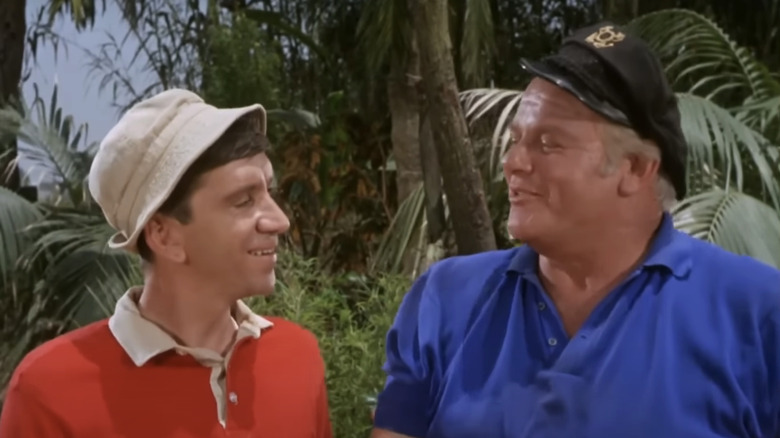 Bob Denver's Gilligan and Alan Hale Jr's Skipper look at each other while standing side by side in Gilligan's Island