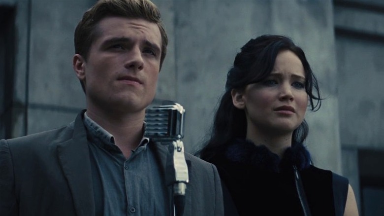 Peeta Mellark and Katniss Everdeen standing in front of a microphone on a stage