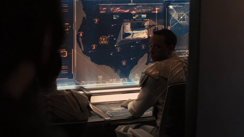 A Capitol officer sitting in front of a monitor with a map of Panem