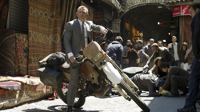 Daniel Craig as James Bond in Skyfall wearing a grey suit on the back of a motorbike