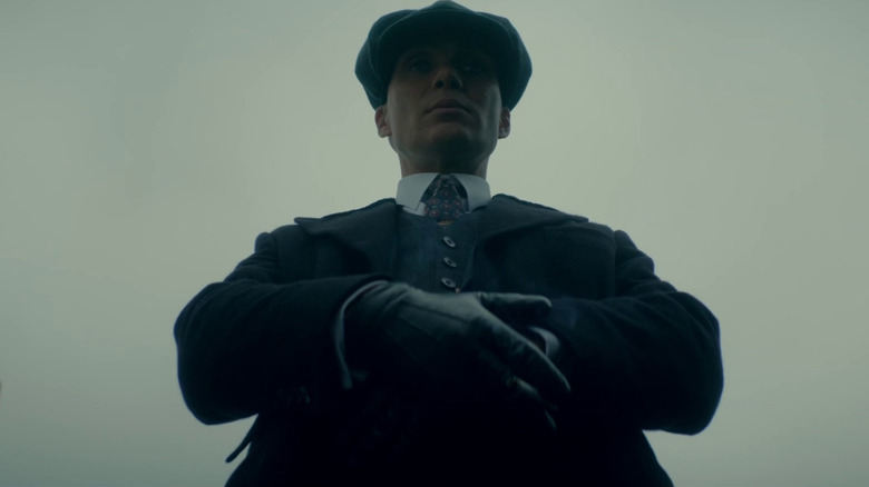 Cillian Murphy as Tommy Shelby folding his hands and staring off-screen ominously in Peaky Blinders