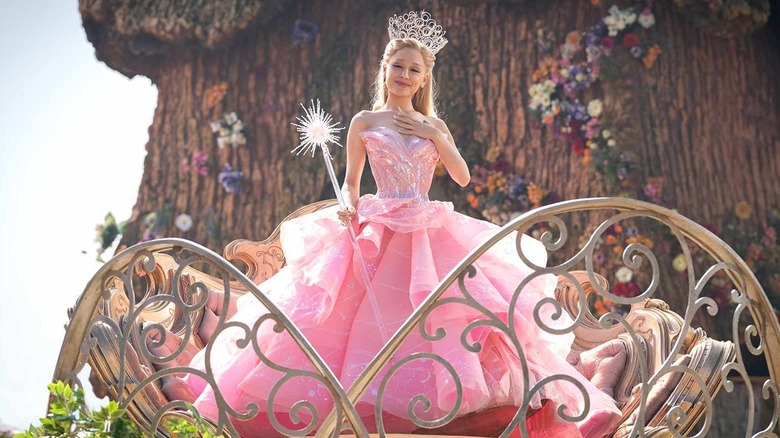 Glinda on a balcony in a pink dress and tiara looking down in Wicked: Part One