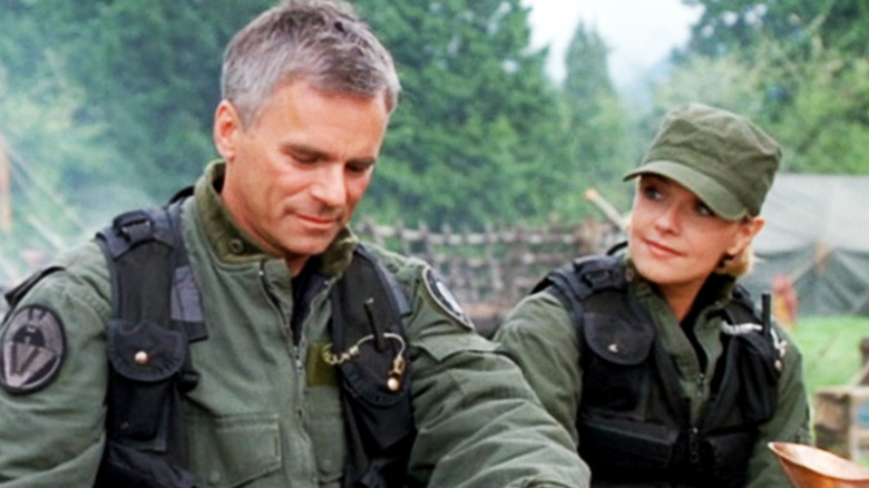 Jack de Richard Dean Anderson y Samantha de Amanda Tapping se sientan uno al lado del otro en una comida para llevar en Stargate SG1