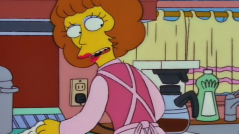 Maude Flanders in an apron, standing in a nice kitchen, looking over her shoulder.